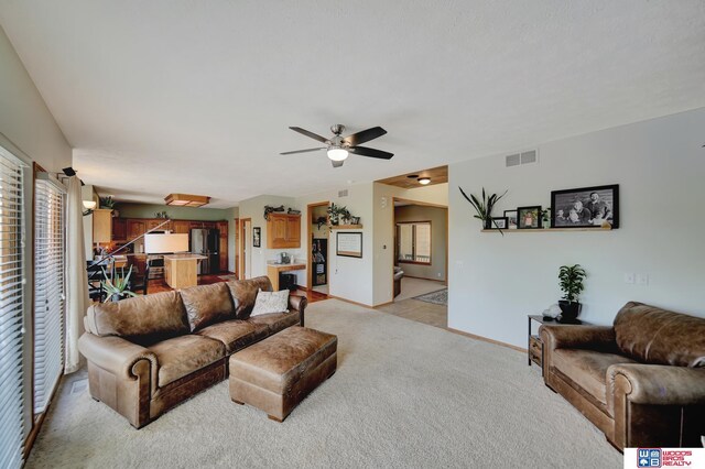 living area featuring healthy amount of natural light, light colored carpet, ceiling fan, and baseboards