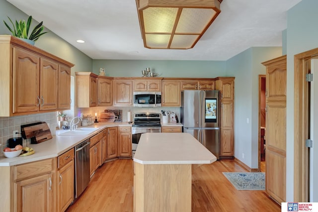 kitchen with stainless steel appliances, a sink, a kitchen island, light countertops, and light wood-style floors