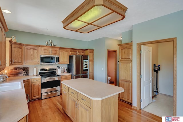 kitchen with stainless steel appliances, a sink, backsplash, a kitchen island, and light countertops