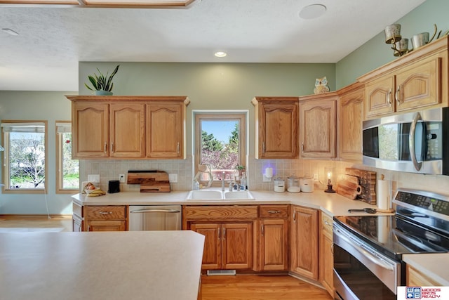 kitchen with stainless steel appliances, a sink, light wood finished floors, healthy amount of natural light, and recessed lighting