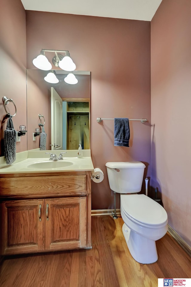 half bathroom featuring wood finished floors, baseboards, vanity, and toilet