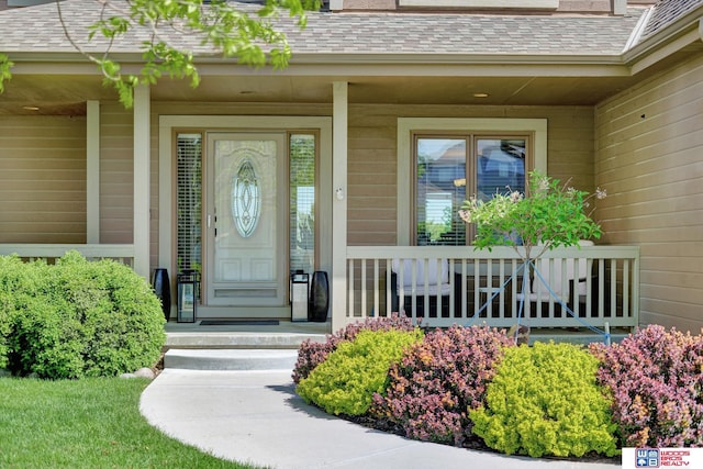 doorway to property with a porch and a shingled roof