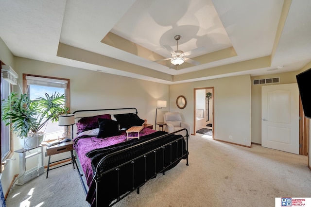 bedroom with a tray ceiling, light carpet, baseboards, and ensuite bathroom