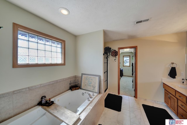 bathroom with vanity, a textured ceiling, a tub with jets, and marble look tiles