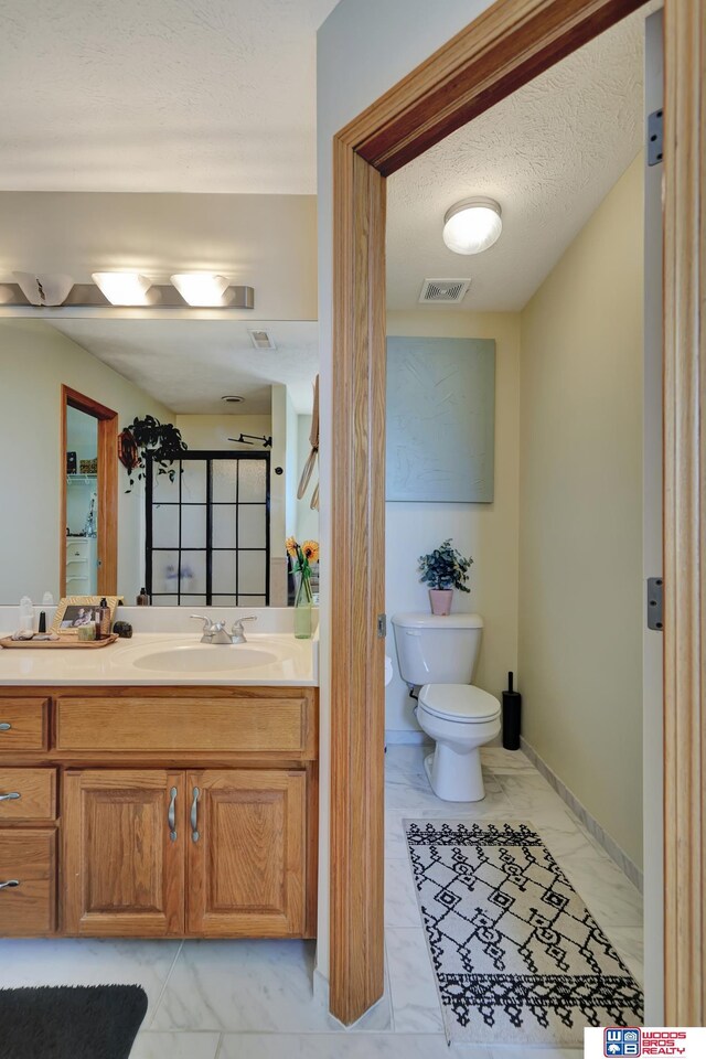 full bath featuring marble finish floors, toilet, a stall shower, vanity, and a textured ceiling