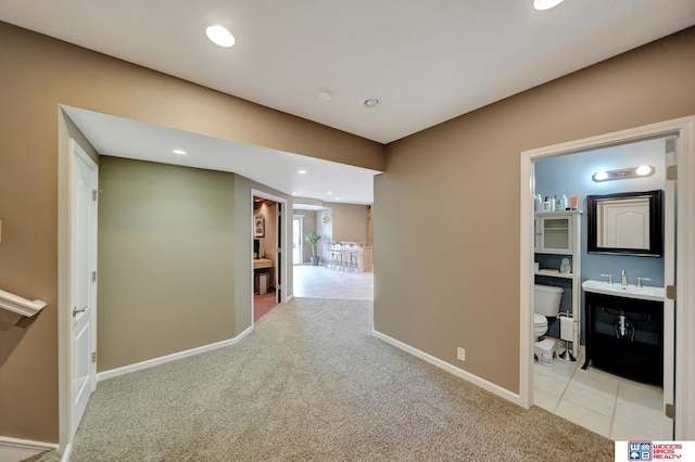 hall featuring carpet, baseboards, a sink, and recessed lighting