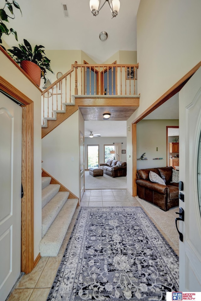 foyer with tile patterned floors, stairs, ceiling fan, and a high ceiling
