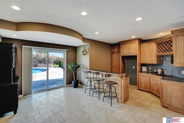kitchen featuring a breakfast bar area, a sink, baseboards, recessed lighting, and dark countertops
