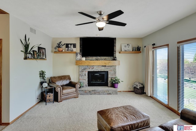 living room featuring baseboards, carpet, a stone fireplace, and ceiling fan
