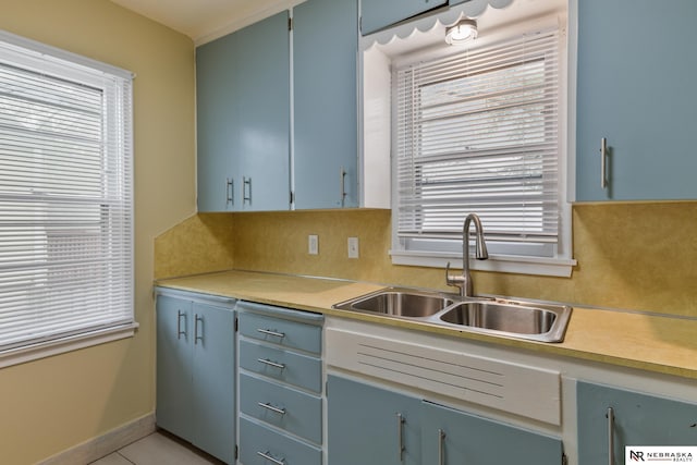 kitchen with a sink, light countertops, backsplash, and blue cabinets
