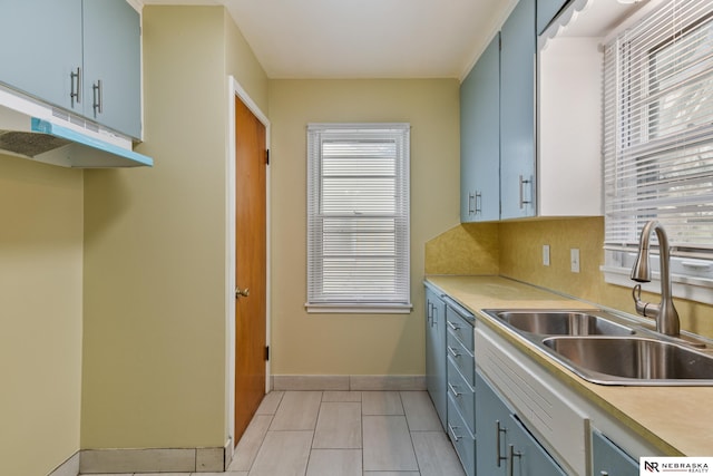 kitchen featuring a sink, light countertops, baseboards, under cabinet range hood, and blue cabinets