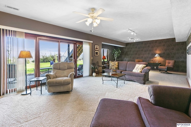 carpeted living room featuring wallpapered walls, rail lighting, visible vents, a ceiling fan, and an accent wall