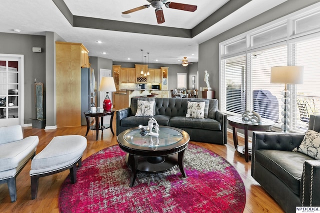 living room featuring light wood finished floors, a ceiling fan, a tray ceiling, and recessed lighting
