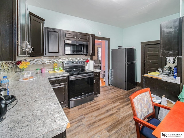 kitchen featuring light wood-type flooring, stainless steel appliances, light countertops, and backsplash
