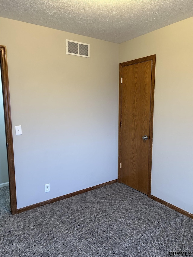empty room featuring a textured ceiling, carpet, visible vents, and baseboards