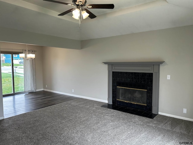 unfurnished living room featuring ceiling fan with notable chandelier, dark colored carpet, baseboards, and a tile fireplace