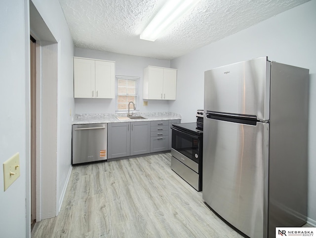 1029 Rose St, Lincoln, NE 68502 - kitchen with appliances with stainless steel finishes, a sink, a textured ceiling, light wood-style flooring, and light countertops