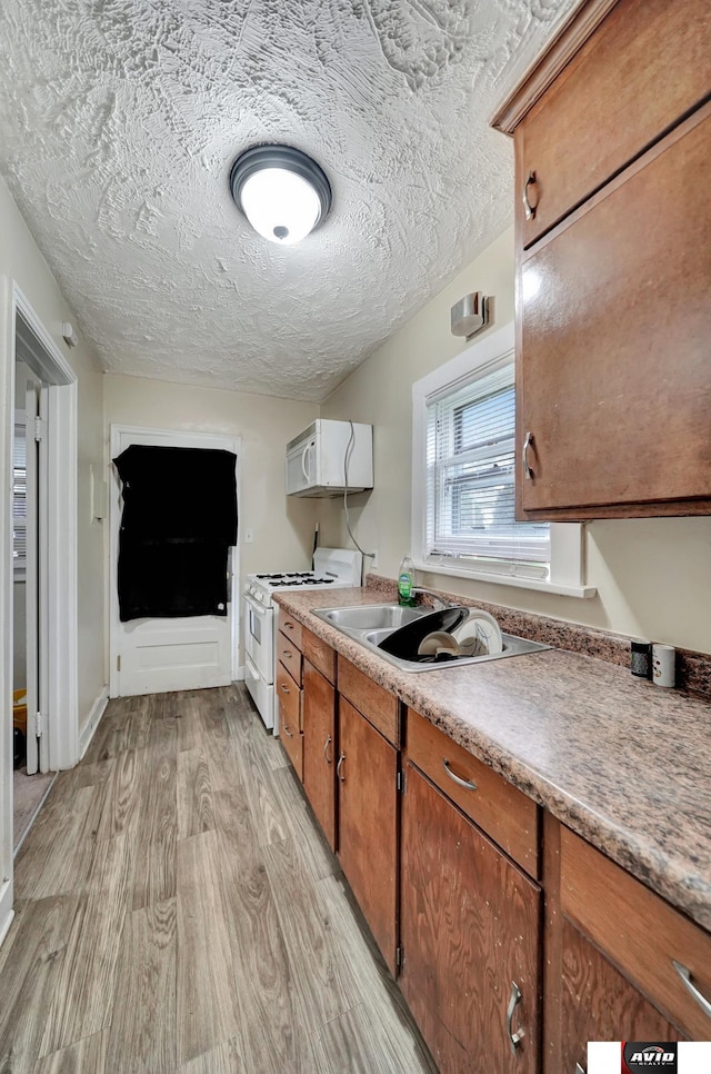 2103 A St, Lincoln, NE 68502 - kitchen with brown cabinetry, a textured ceiling, a sink, light wood finished floors, and white appliances