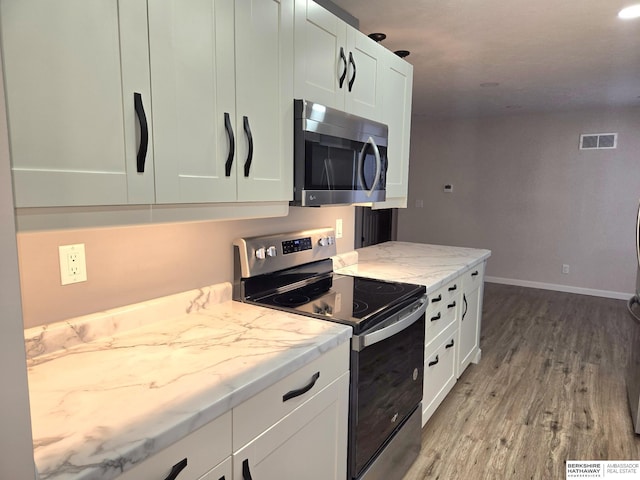 kitchen featuring visible vents, light wood-style flooring, light stone counters, white cabinetry, and appliances with stainless steel finishes