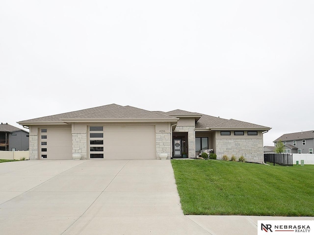 prairie-style home featuring a garage, fence, a front yard, stone siding, and driveway