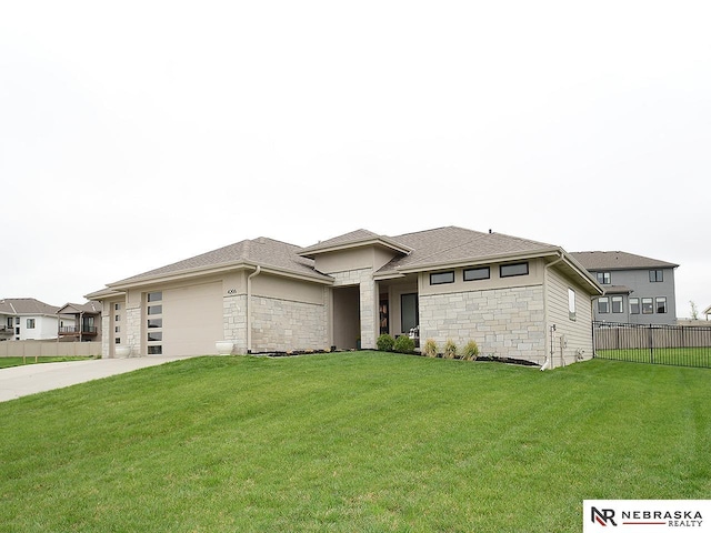 prairie-style home with fence, a front lawn, concrete driveway, an attached garage, and stone siding