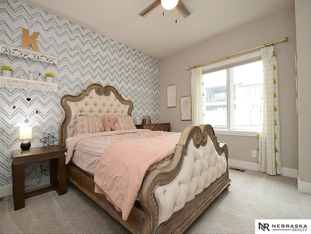 bedroom featuring ceiling fan, light colored carpet, visible vents, baseboards, and an accent wall