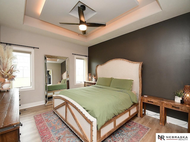 bedroom featuring baseboards, a ceiling fan, a raised ceiling, and wood finished floors