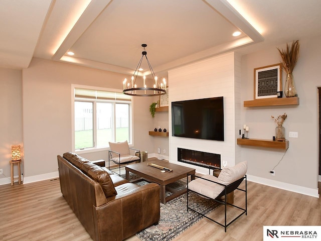 living area with an inviting chandelier, baseboards, wood finished floors, and a tray ceiling