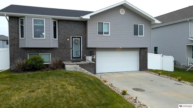 bi-level home featuring a front lawn, fence, brick siding, an attached garage, and driveway