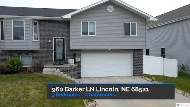 split foyer home featuring brick siding, an attached garage, fence, and a front lawn