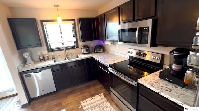 kitchen featuring light stone countertops, dark wood finished floors, dark brown cabinets, a sink, and stainless steel appliances