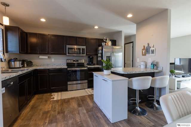 kitchen featuring dark wood-style flooring, appliances with stainless steel finishes, a breakfast bar, a sink, and a peninsula
