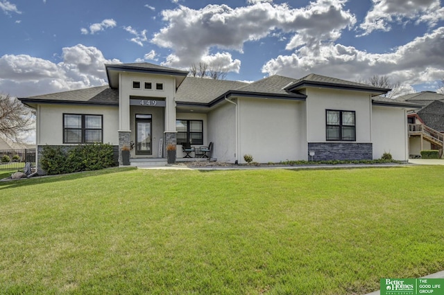prairie-style home featuring stucco siding, a front lawn, roof with shingles, and stone siding
