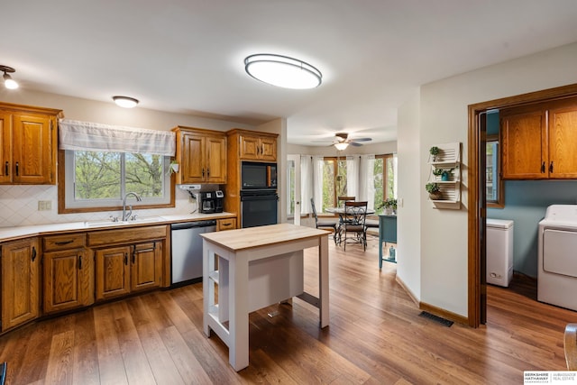 kitchen featuring visible vents, washing machine and dryer, wood finished floors, a sink, and black appliances