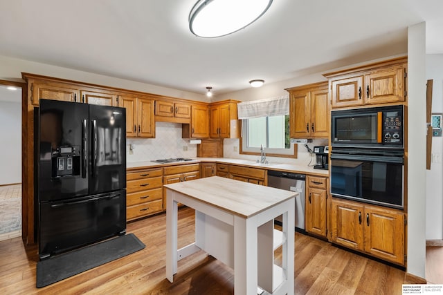 kitchen featuring light countertops, light wood-style flooring, black appliances, and decorative backsplash
