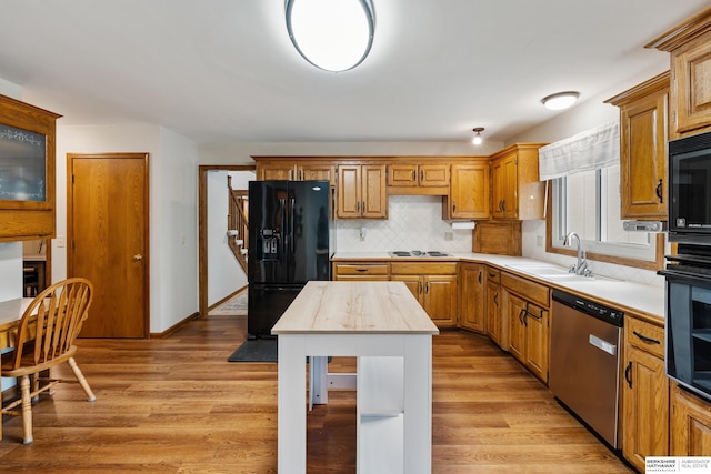 kitchen featuring a kitchen island, tasteful backsplash, a sink, light wood-style flooring, and black appliances