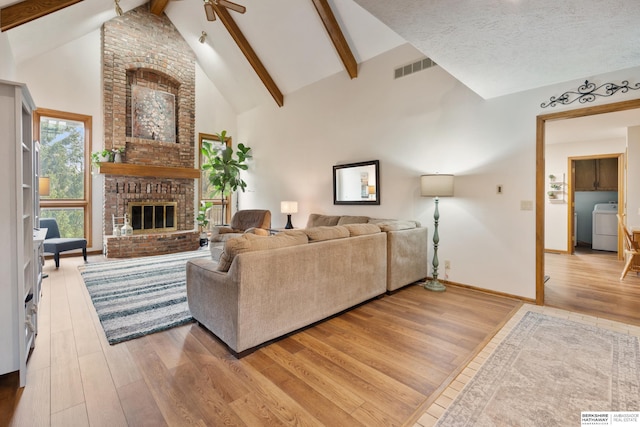 living room with visible vents, washer / dryer, beam ceiling, a fireplace, and light wood-type flooring
