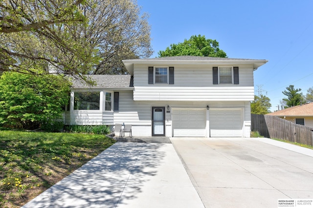 split level home with concrete driveway, fence, a shingled roof, and a garage