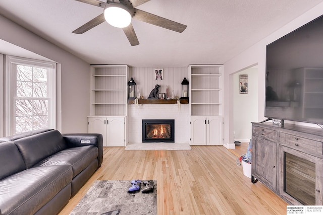 living area featuring a ceiling fan, light wood-style flooring, and a glass covered fireplace