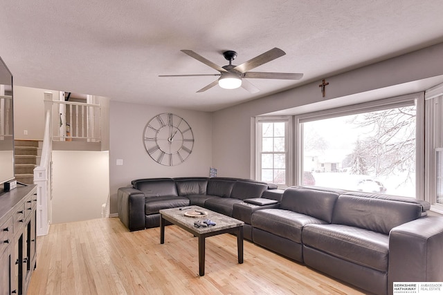 living area with light wood-style floors, a textured ceiling, ceiling fan, and stairs