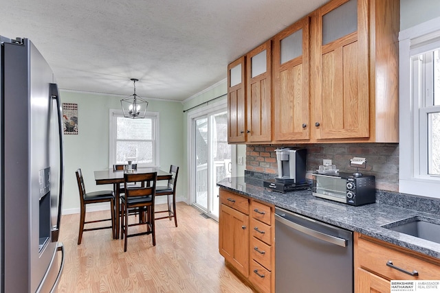kitchen with appliances with stainless steel finishes, light wood-style floors, a chandelier, dark stone counters, and decorative backsplash