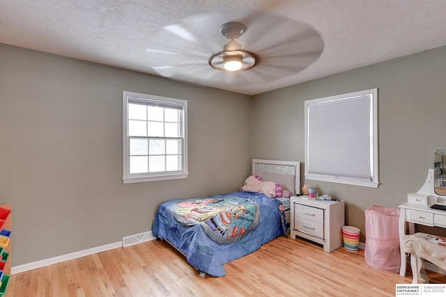 bedroom featuring ceiling fan, a textured ceiling, baseboards, wood finished floors, and visible vents