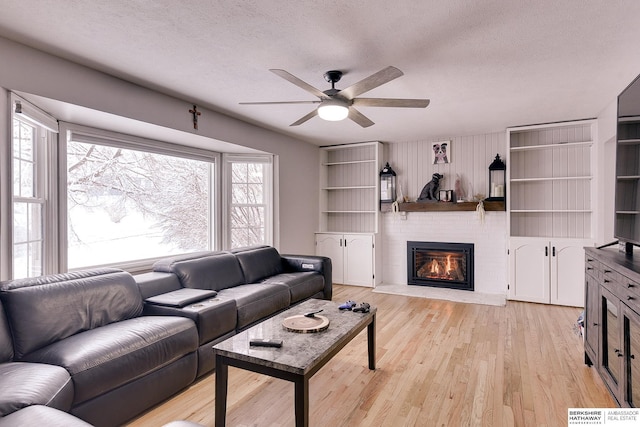 living area featuring ceiling fan, a brick fireplace, light wood-type flooring, and a textured ceiling