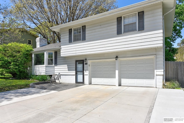 split level home featuring fence, a chimney, driveway, and a garage