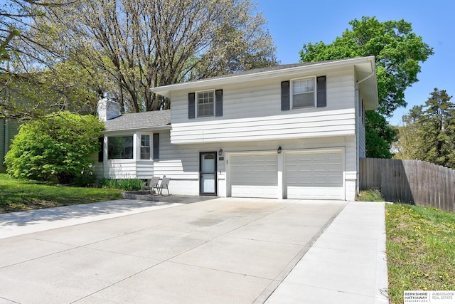 split level home with concrete driveway, fence, a chimney, and a garage