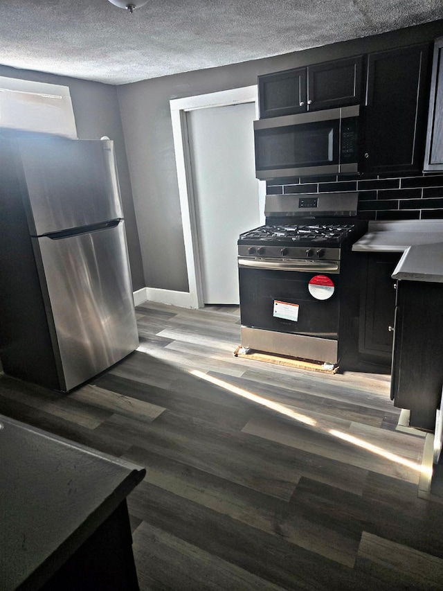 kitchen featuring tasteful backsplash, baseboards, stainless steel appliances, and dark cabinets