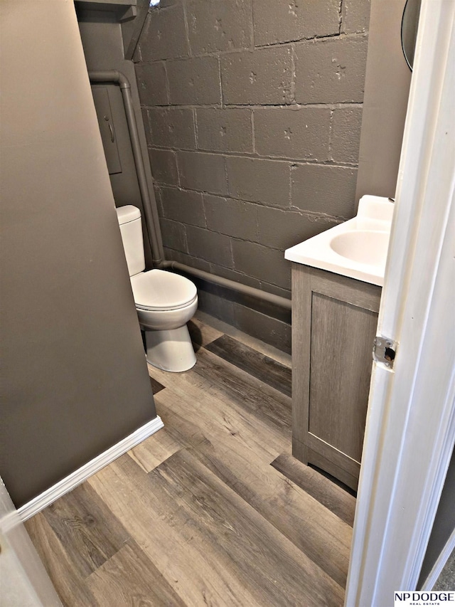 full bathroom featuring concrete block wall, wood finished floors, toilet, vanity, and a shower