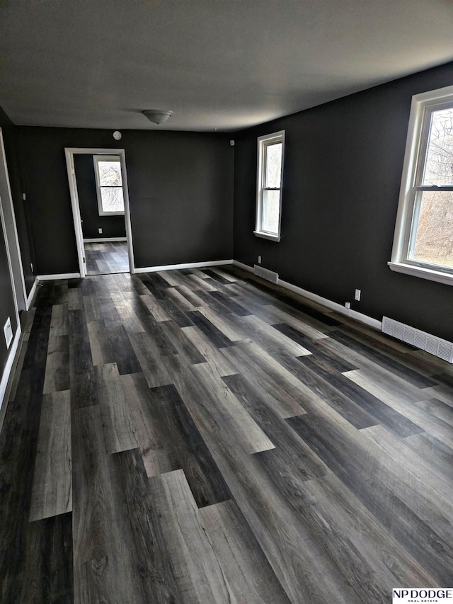 unfurnished room with baseboards, visible vents, and dark wood-type flooring