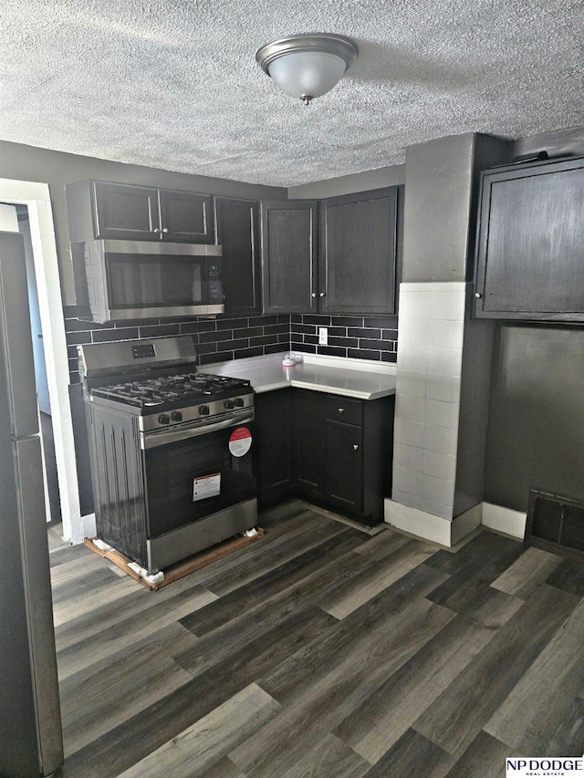 kitchen featuring a textured ceiling, tasteful backsplash, dark wood-style flooring, light countertops, and appliances with stainless steel finishes