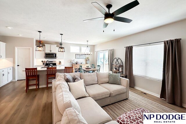 living room featuring dark wood finished floors, baseboards, ceiling fan, and visible vents